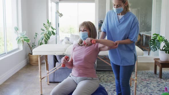 Female health worker assisting senior woman to exercise with dumbbells at home alt