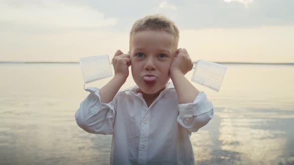 a Cheerful Child Indulges in a Pond Putting Glasses to His Ears and Grimacing alt