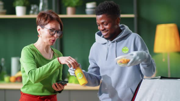 Cheerful Black Deliveryman Unloading Healthy Food for Woman alt
