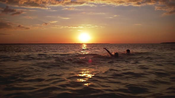 Silhouettes of Two Young Boys 1012 Swimming Together in Sea During Amazing Dusk in Slow Motion alt