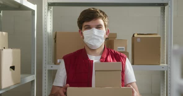 Man Wearing Red Vest Holding Parcels Employee of Warehouse in Medical Face Mask Holds Delivery Boxes alt