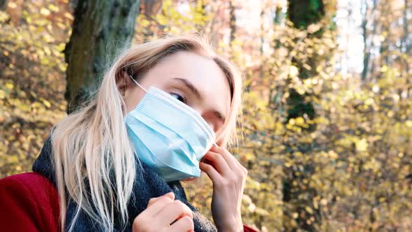 Portrait of a young beautiful woman putting on Corona safety mask amidst orange brown autumn forest alt