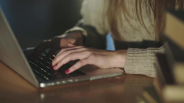 View of Female Hands Typing on Laptop Keyboard at Desk with Books on Dim Light alt