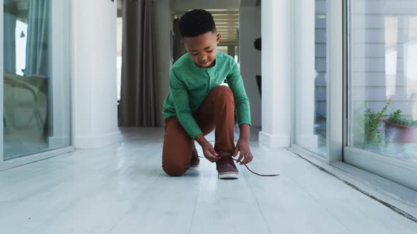 African american boy standing in hallway tying his shoes alt