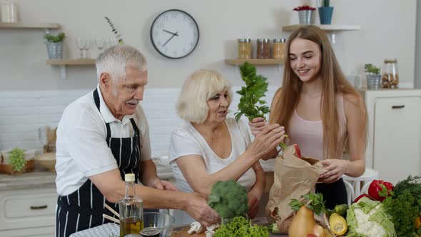 Senior Couple in Kitchen Receiving Vegetables From Granddaughter. Healthy Raw Food Nutrition alt