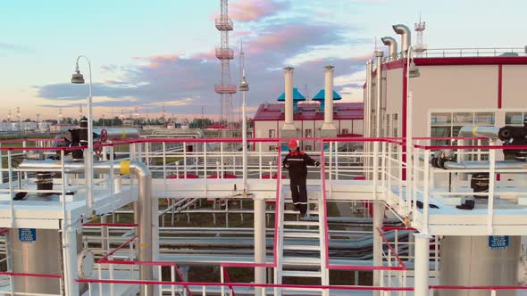 The Oil and Gas Industry a Worker on Tanks for Cleaning Oil From Gas Descends a Metal Ladder alt