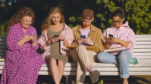Young Man and Women Sitting on Bench Outside Using Mobile App or Consulting Internet alt
