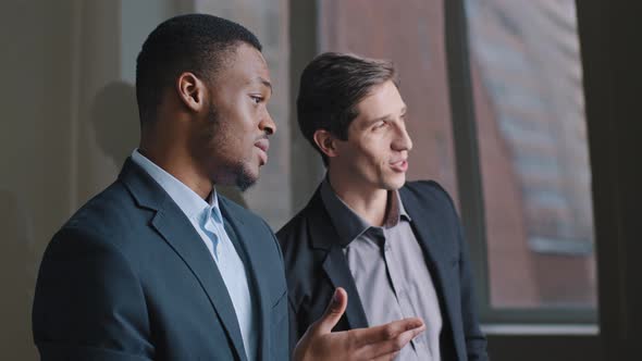 Two Serious Young Businessmen Multiracial Colleagues Standing in Office Looking Out Window Caucasian alt