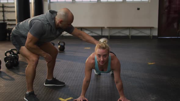 Male trainer correcting form of fit caucasian woman while push up exercise at the gym alt