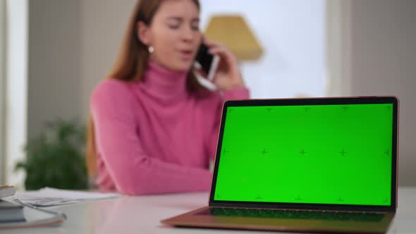 Green Screen of Laptop with Blurred Woman Talking on Phone at Background alt