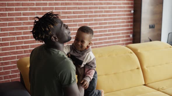 African Male and His Little Son Spend Time Together Fooling Around on Sofa alt