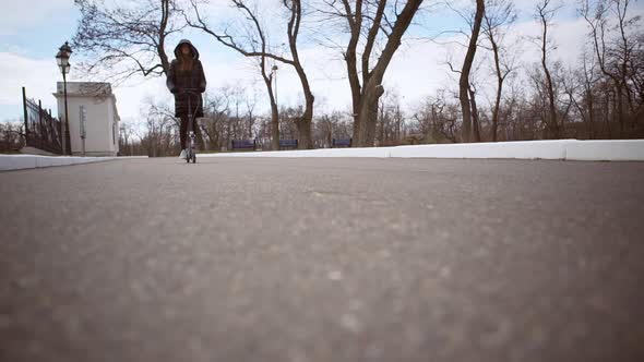 Caucasian Girl in Winter Parka Riding Kick Scooter Along the Street in Slowmotion alt