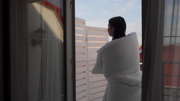 Woman in a White Blanket Stands in the Doorway with a Cup of Tea alt