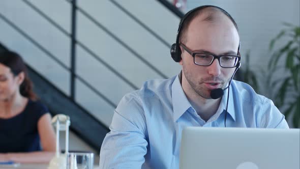 Joyful Call Centre Agent with His Headset Talking Looking at Laptop alt