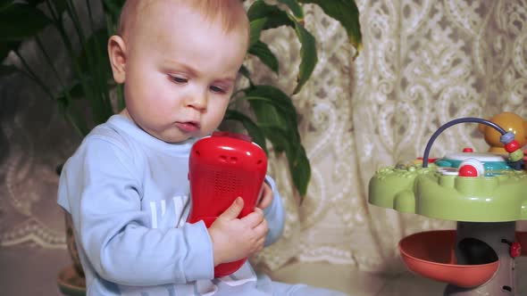 Concentrated Little Girl Holds a Red Toy in Her Hands and Carefully Examines It