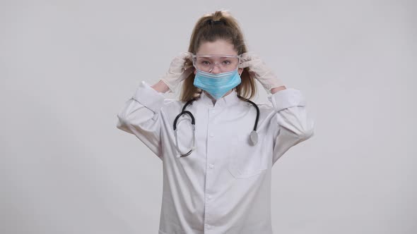 Little Caucasian Nurse Doctor Putting on Medical Covid19 Face Mask Looking at Camera alt