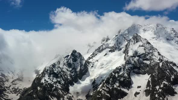 Air Flight Through Mountain Clouds Over Beautiful Snowcapped Peaks of Mountains and Glaciers alt