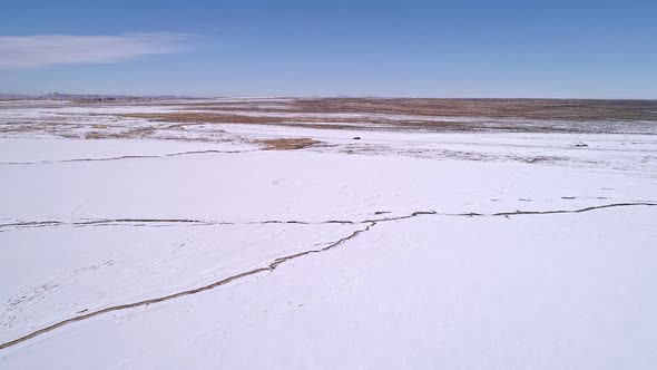 Flying over flat desert snowy landscape towards vehicle on road alt