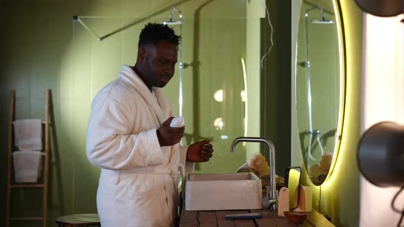 Side View Positive Handsome African American Man in Bathrobe Turning on Music on Smartphone Applying alt