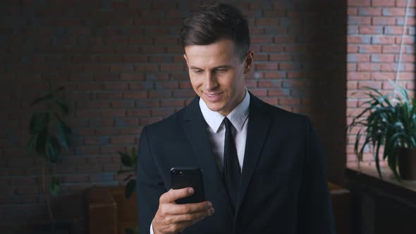 Young Confident Businessman Enjoying Using Mobile Apps at His Smart Phone