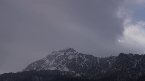Dense clouds over the rocky peak. Windy winter weather. Slow zoom in alt