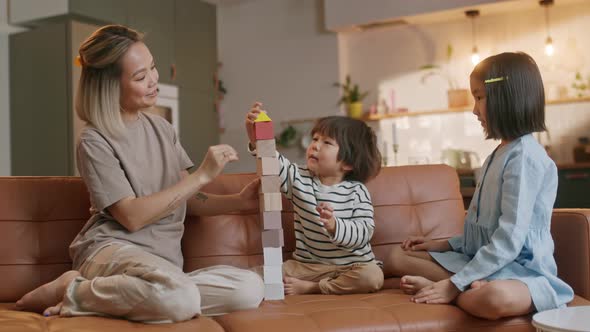 Happy Asian Young Mother and Two Little Children Sitting at Sofa and Playing Together alt