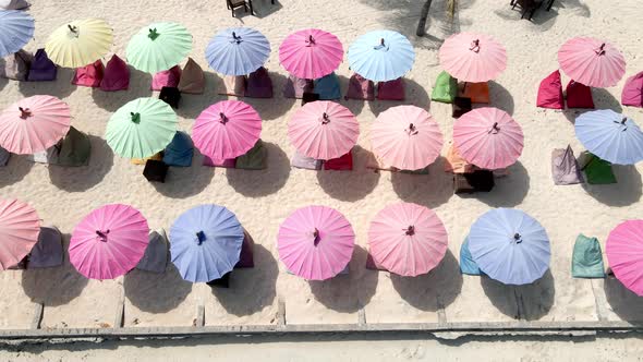 Aerial top down view of young girl lying at beach during summertime in front of colorful umbrellas. alt