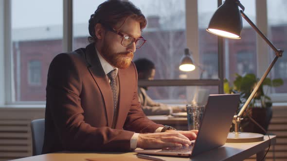 Caucasian Businessman Working on Laptop at Office Desk in the Evening alt