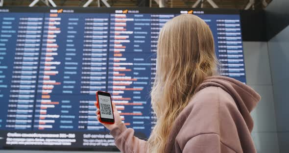 Passenger in the Airport Looking at QR Code on the Screen of Smartphone Mobile alt