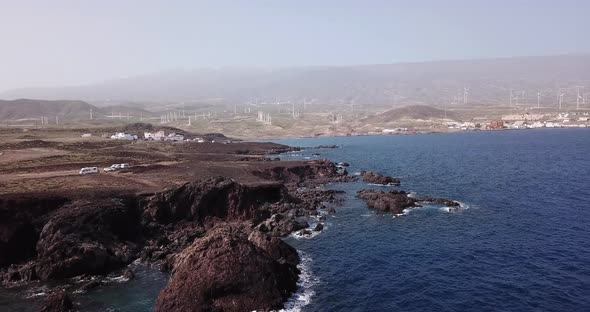 Beautiful coastline aerial view with cliffs and rocks and blue. Town and windmills in background. alt