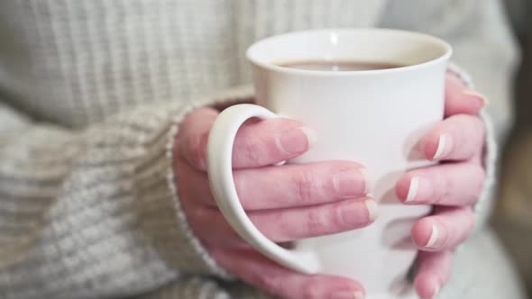 The woman is drinking freshly brewed hot tea. Warms hands with a mug of tea.