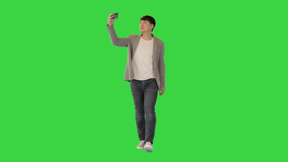 Young Asian Man Walks Makes a Photo and Smiles on a Green Screen Chroma Key alt