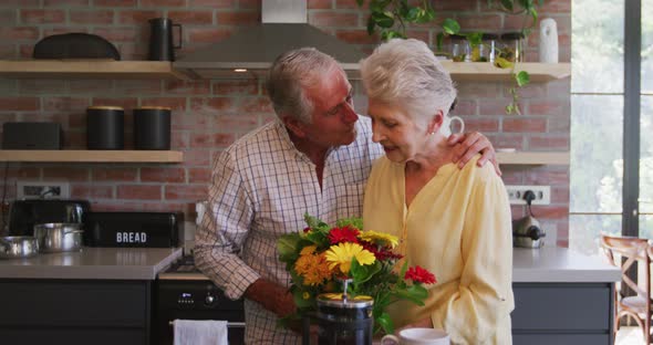 Senior Caucasian husband offering flowers to his wife, hugging and smiling alt