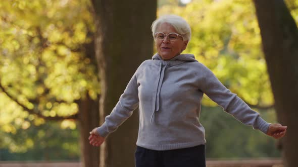 Senior Caucasian Woman Jumping Moving Her Hands Doing Sports in the Park Healthy Lifestyle Active alt