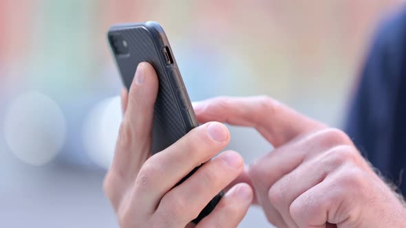 Outdoor Close Up of Hands of Middle Aged Man Scrolling on Smartphone alt