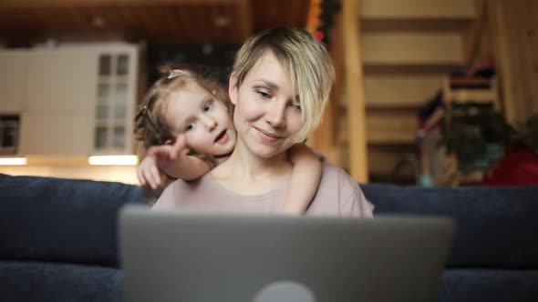 Woman Is Trying To Work on Laptop with Her Daughter Cuddling Her in Living Room