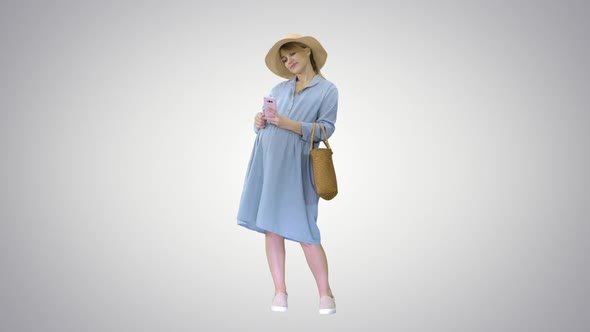Happy Pregnant Woman in Blue Dress and Hat Using Her Smartphone on Gradient Background. alt