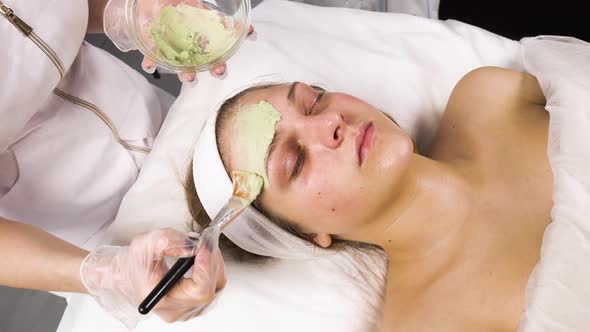 The Cosmetologist Applies a Green Natural Ecological Mask to the Client's Face