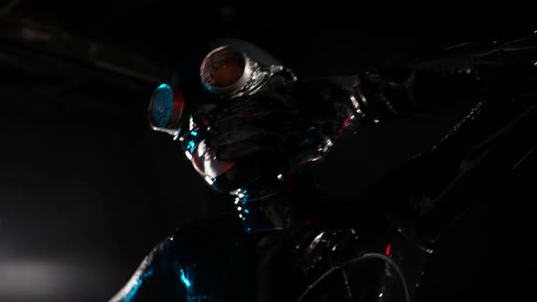 a Woman in a Black Latex Suit Helmet and Glasses Touches Head with Gloved Hands and Bends Against a alt