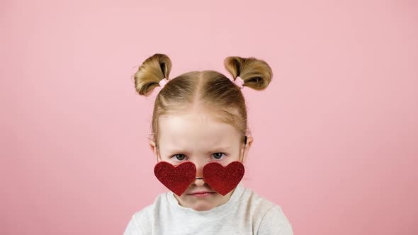 Funny Angry Little Blonde Girl in Red Heart Shape Sunglasses on Pink Background alt