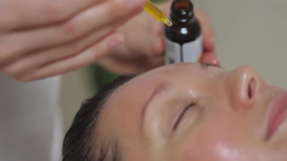 Applying Massage Oil on the Forehead of a Beautiful Brunette Woman in Spa Salon alt