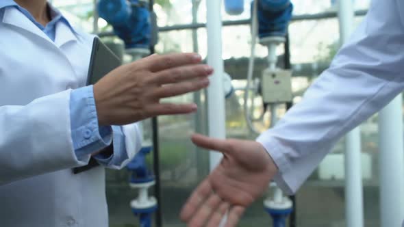 Male and Female Engineers in White Coats Shaking Hands at Factory, Cooperation