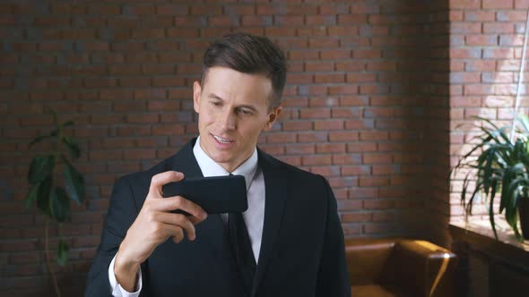 Portrait of Young Businessman Man Enjoying Watching Funny Videos on a Smartphone in a Modern Office