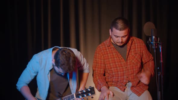 Two Men Sit on Chairs in the Recording Studio and Record a Song - One of Them Picks Up a Guitar alt