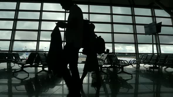 Travelers Walking Along Window in Airport Terminal, People Silhouettes Walking.