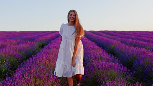 Young Woman in White Dress Walking Through a Lavender Field on Sunset