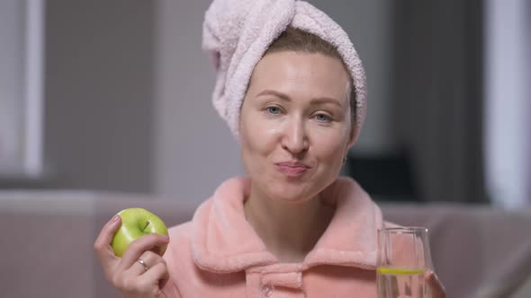 Slim Positive Young Woman Eating Apple Drinking Detox Lemon Water at Home in the Morning alt