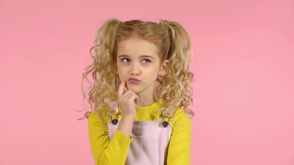Blond Female with Two Ponytails Is Concentrated on Thinking, Touching Her Face with Finger alt