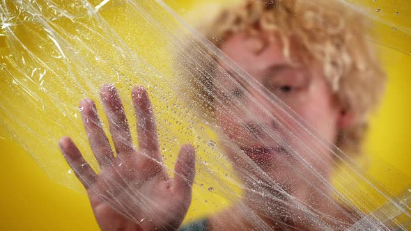 Closeup Male Caucasian Hand Touching Wet Food Film with Blurred Man at Yellow Background alt