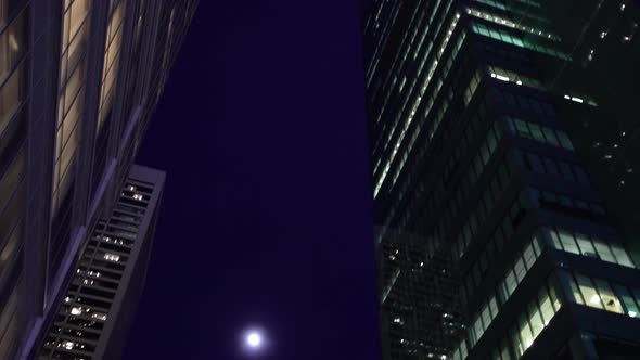 Looking up at full moon and tall skyscrapers at night